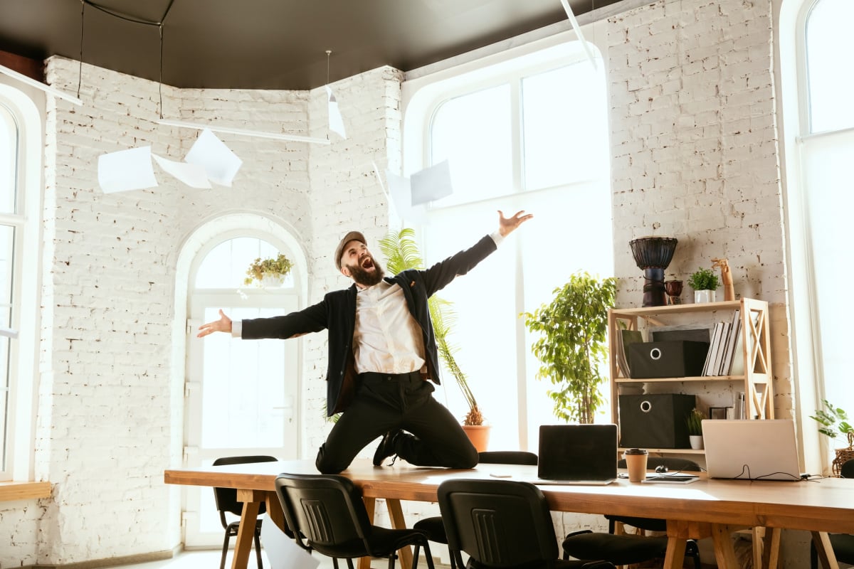 A happy man standing on a table, throwing papers in the air, symbolizing the freedom from tedious manual paperwork through automated document processing solutions.